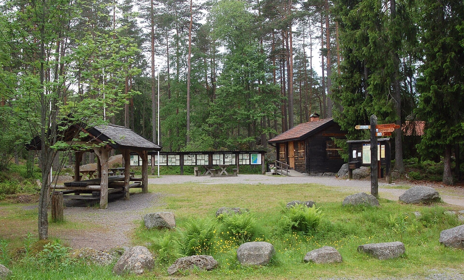 A rest area in Tiveden National Park with a picnic shelter, information boards, a timber cabin and a signpost pointing to Trollstigen and Oxaberget.